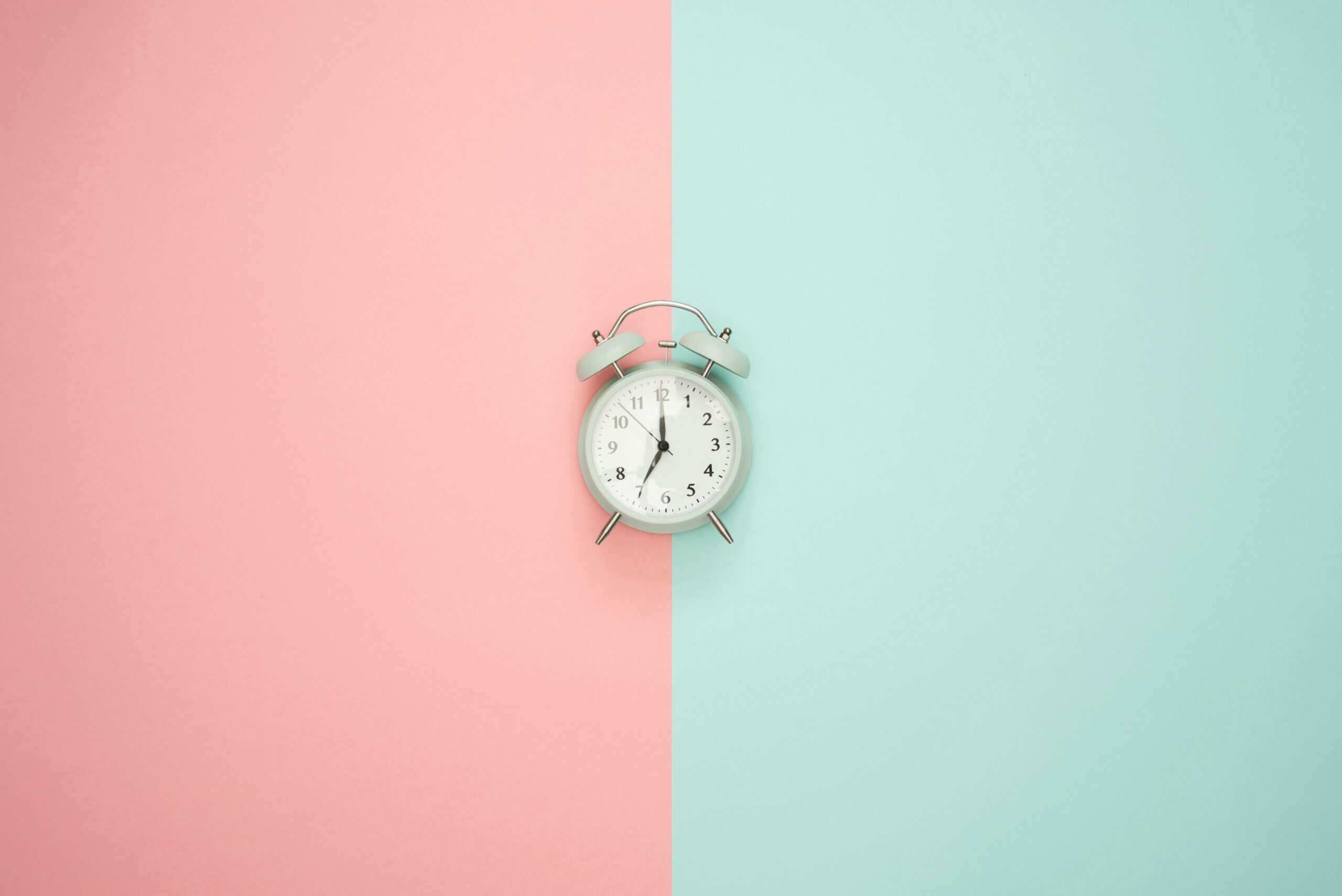 A vintage round clock on a split pastel pink and blue background.