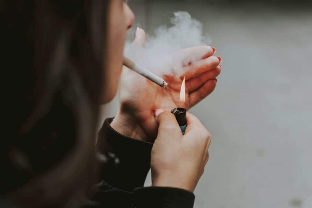 Close-up of a woman lighting a cigarette outdoors with a lighter, smoke visible.