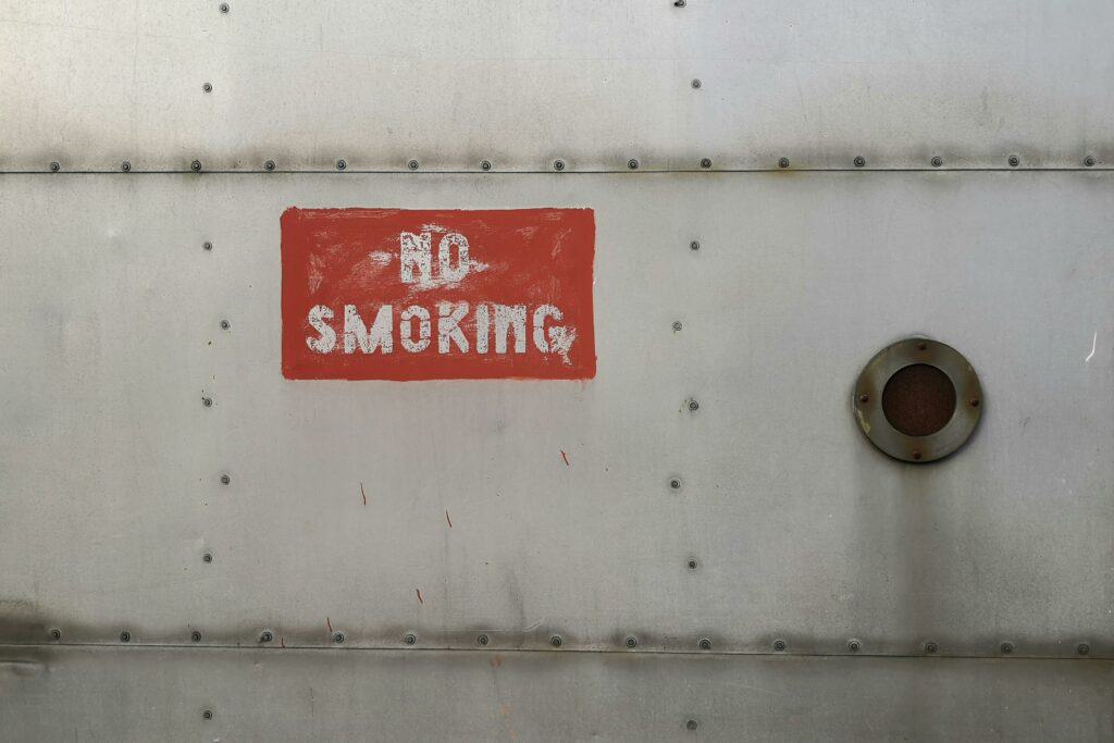 Close-up of a rusty 'No Smoking' sign painted on a metallic surface with rivets.